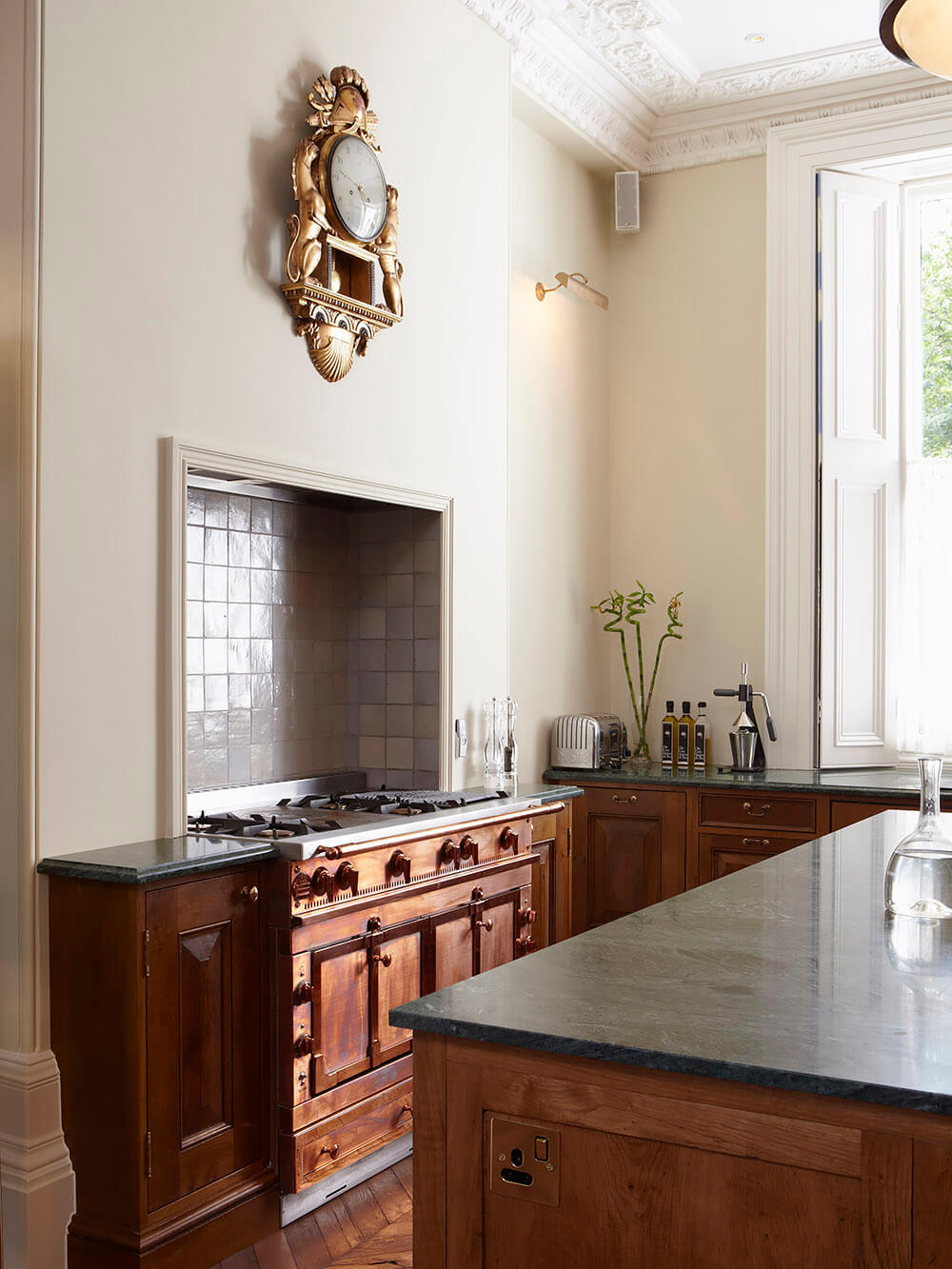 Luxury bespoke kitchen in Ladbroke Grove with parquet floor, wooden cupboards and antique clock on the wall.