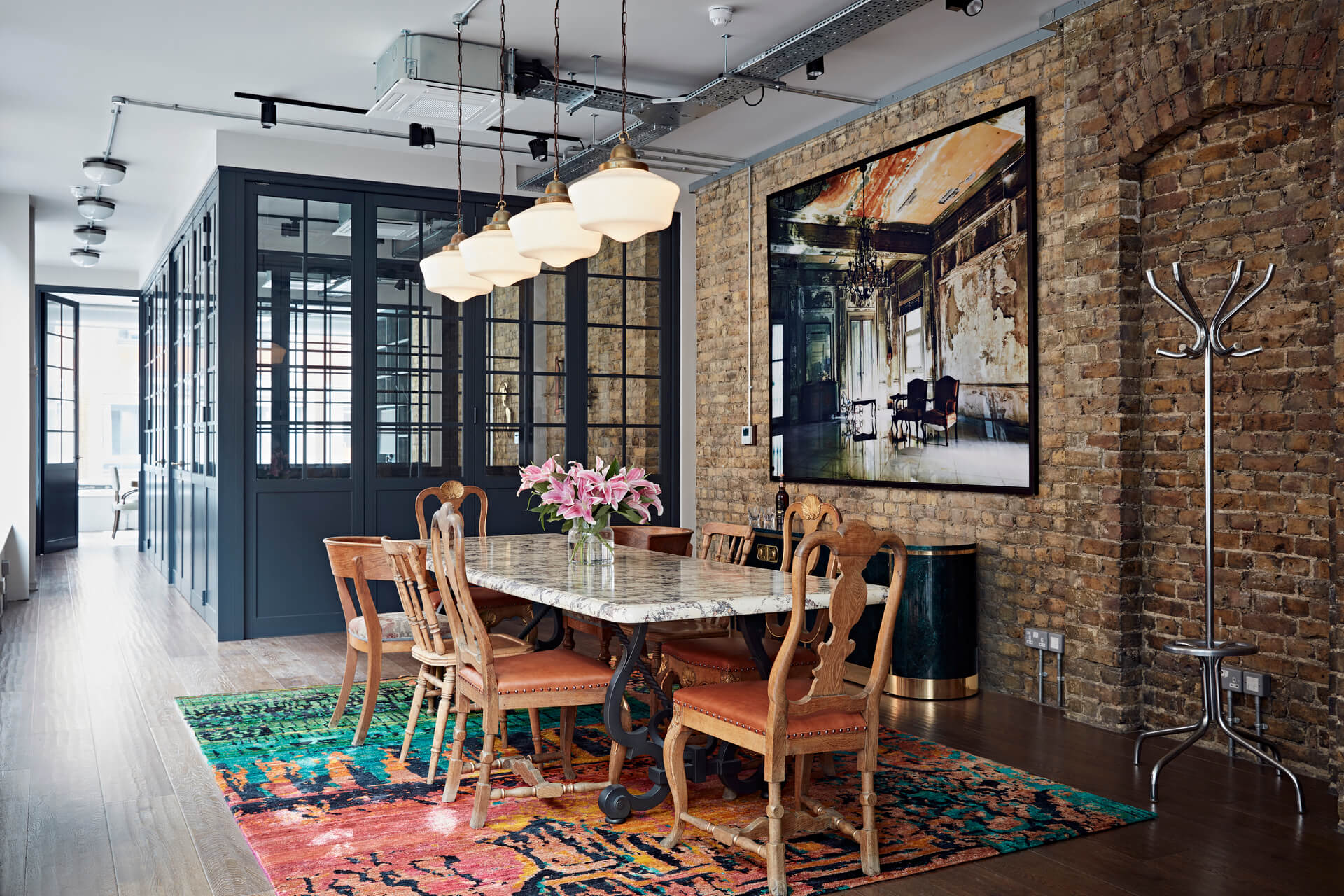 Luxury interior design of London office with marble table, vintage wooden chairs, colourful rug and large artwork on the exposed brick wall.