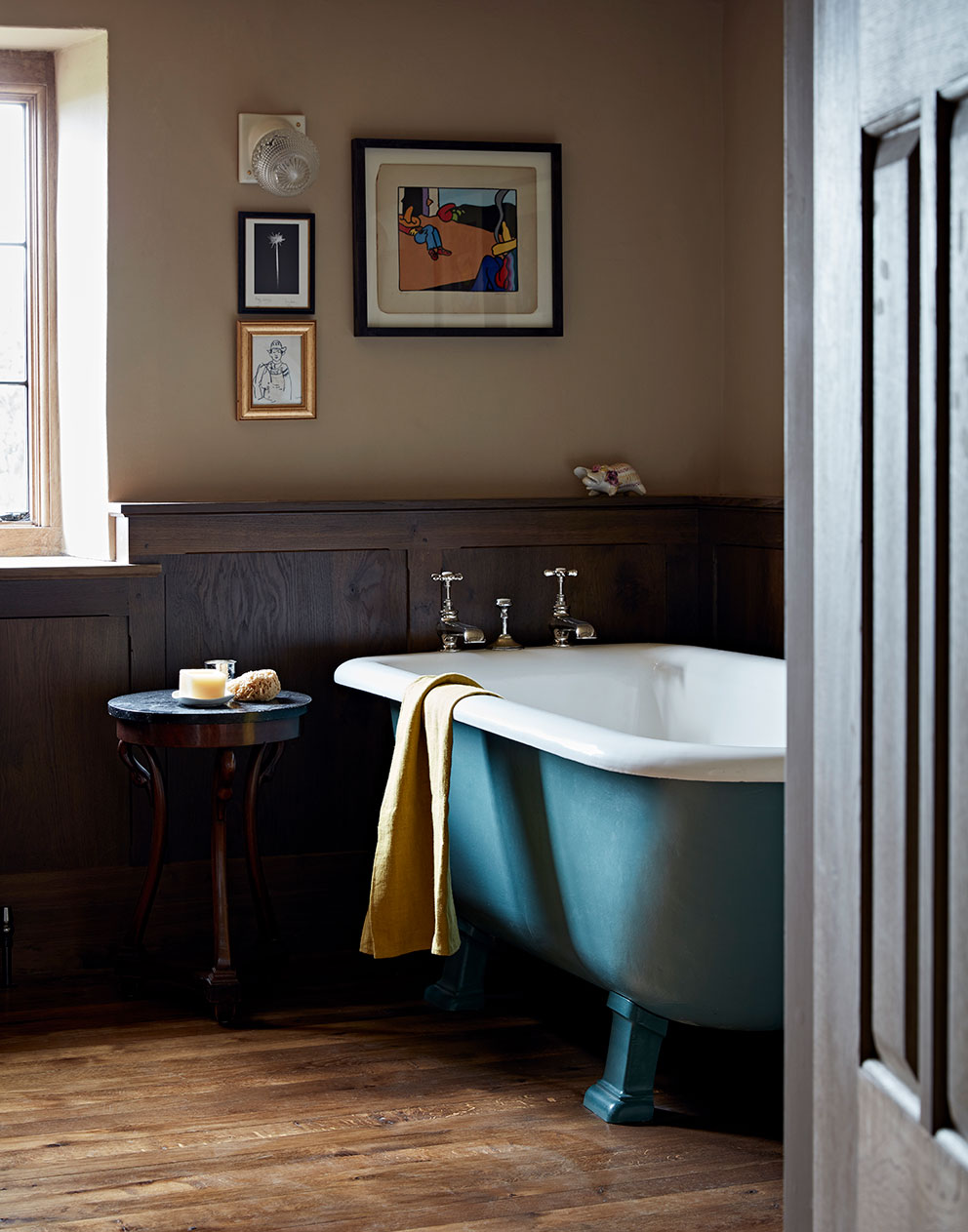 Bathroom in a luxury rural home with a stunning roll top bath surrounded by wood panelling and unique artworks.