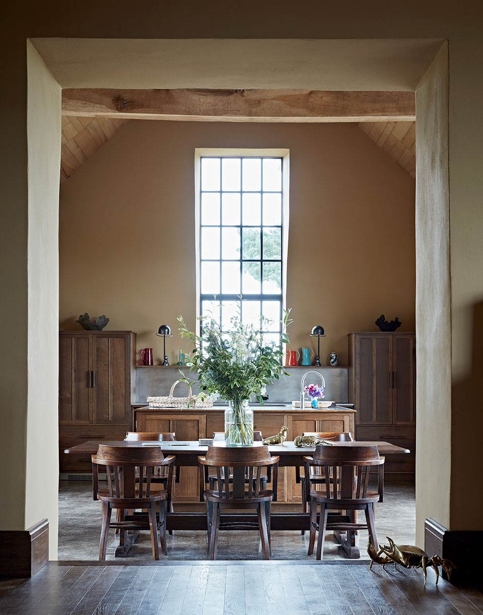 A view of the stunning bespoke kitchen / diner of a luxury rural home with double-height ceilings, dark wooden furniture and soft muted natural walls.
