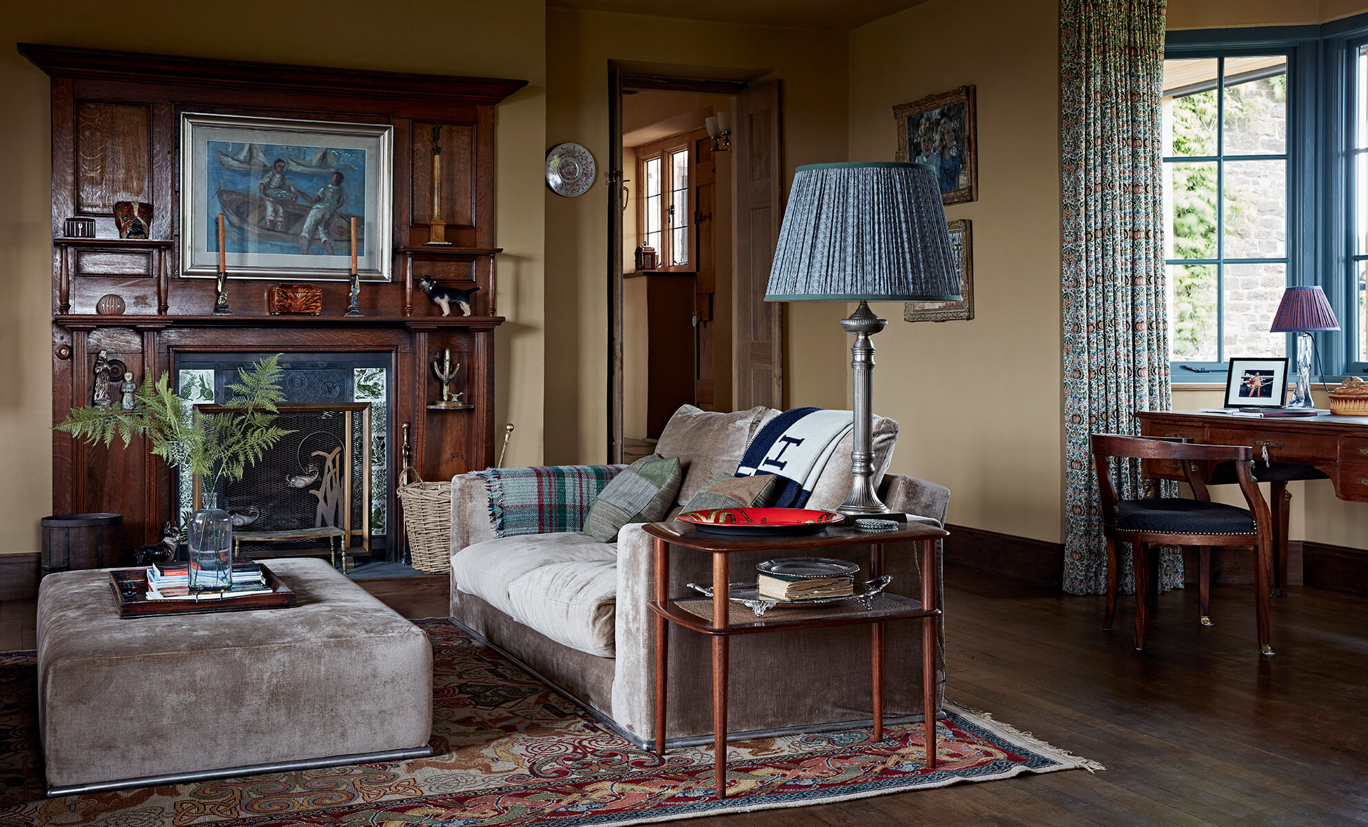 The living room in this luxury farmhouse conversion with a velvet sofa and matching ottoman beside a dark wood and blue fireplace.