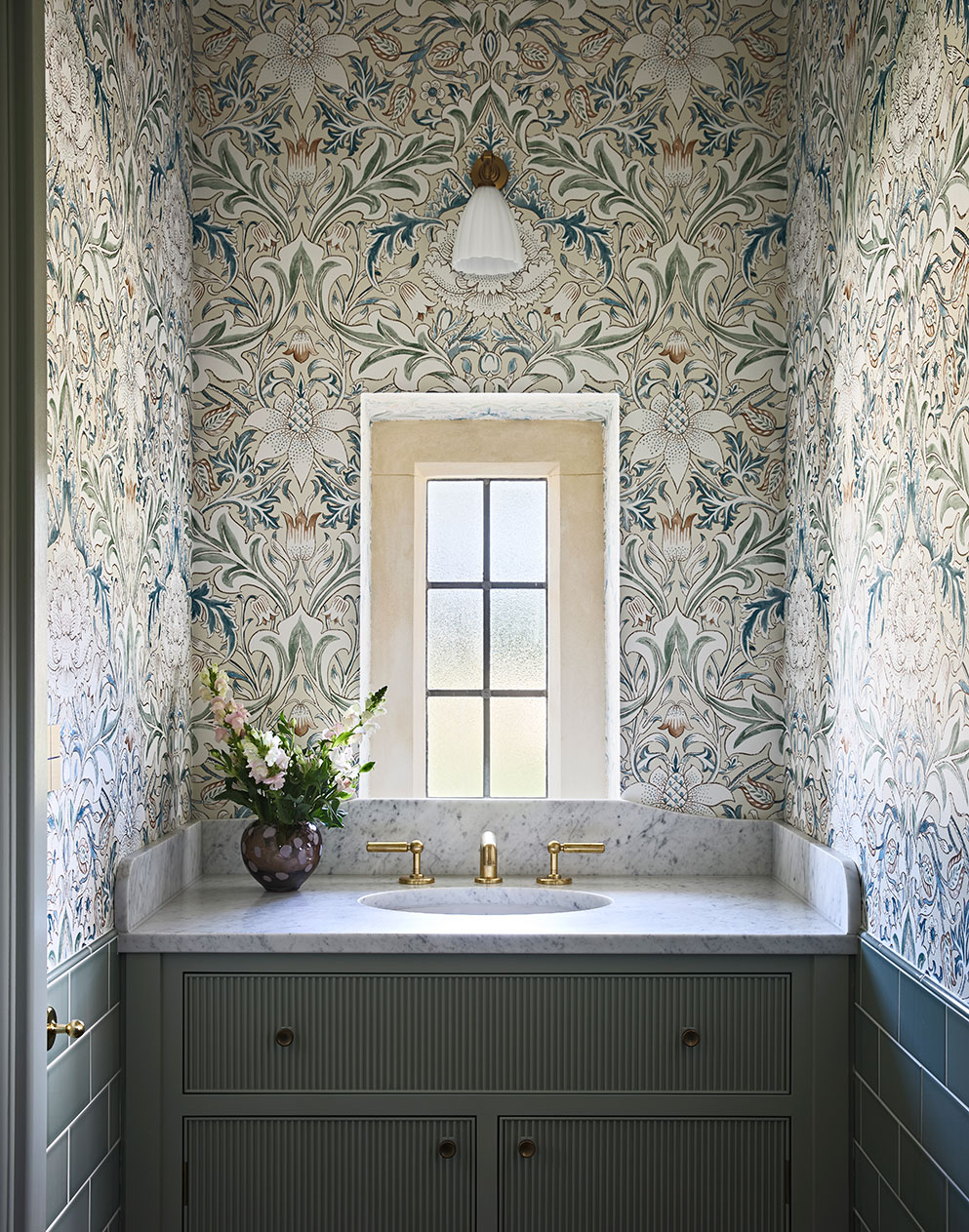 Arts and craft wallpaper in a small room with a marble basin, elegant glass wall light and teal tiles.