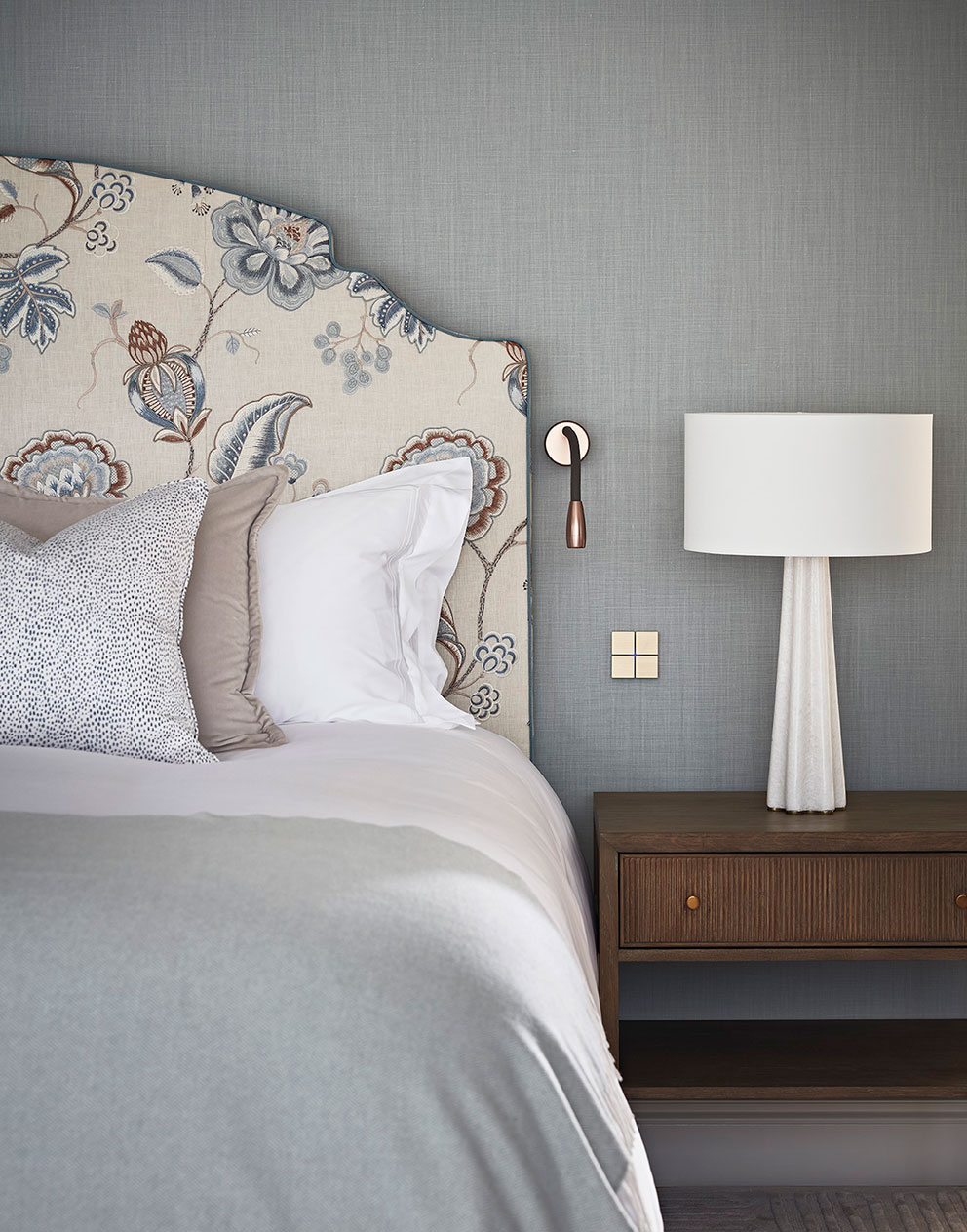 An upholstered headboard with cushions on the bed next to a wooden bedside table.