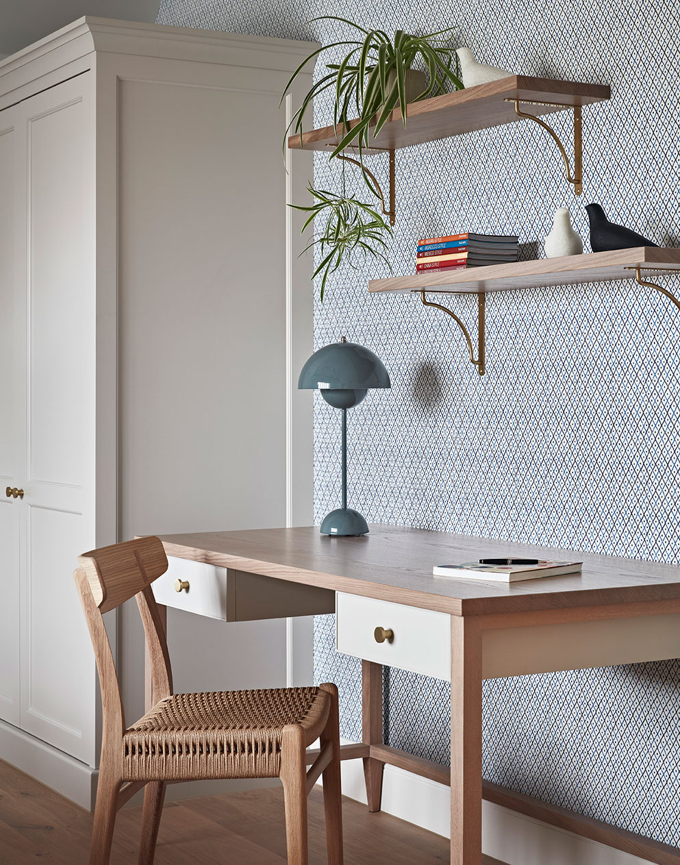 Calm, Scandinavian and minimalist desk with woven chair, some shelves and a teal table lamp.